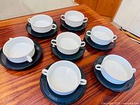 Seven white double-handled bowls on black underplates displayed on table