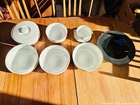 Full set displayed on table showing all eight pieces including white ribbed bowls, lidded casserole, gravy boat with saucer, and black serving bowl