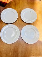 Top view of four white Rosenthal dinner plates on wood surface