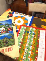 Three tea towels on table showing 1975 calendar, New Zealand scene, and floral design