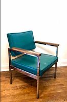 Full view of turquoise vinyl armchair on wood floor