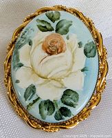 Front view of brooch showing floral painting and gold-tone frame