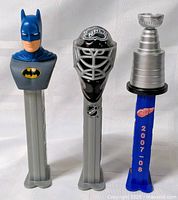 Front view of three PEZ dispensers: Batman, NHL goalie mask, Stanley Cup