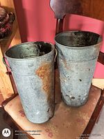 Two tall galvanized steel buckets with handles showing rust and wear placed on a chair
