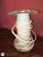 Full view of metal spool with white wire against pink wall