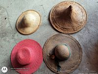 Four woven straw hats laid out: conical, flat-crown, pink wide-brim, ribboned wide-brim