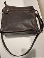 Full view of front/back of brown leather handbag showing zip pocket and strap