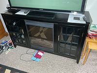 Front view of black media cabinet with electric fireplace insert and side glass doors