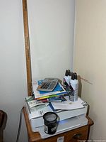 Overall view of printer with accessories stacked on top including calculator, Dust-Off cans, yardstick, mesh cup