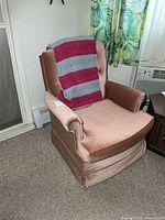 Dusty rose swivel rocker with afghan draped over back, left/front view