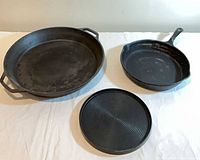 Three cast-iron pieces: large double-handle skillet, long-handle skillet, round griddle