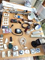 Overview of assorted electrical supplies on tabletop: fluorescent fixtures, timers, work lights, power strips, adapters, wall plates, cords