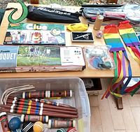 Tabletop view: Franklin croquet box, Clue board game, Bananagrams pouch, ring toss bag, badminton bag, rainbow streamers, assorted croquet pieces in bin