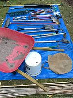 Overall lot on tarp showing wheelbarrow, bucket, long-handled tools and accessories
