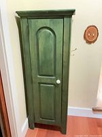 full front view of green stained pine cabinet showing arched-panel door and white knob