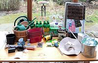 Overall view of gardening items on table including watering cans, LiquaFeed bottles, seed trays, planters, grow light, sunhat