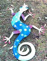 Full view of painted metal gecko lying on grass
