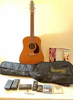 Full view of guitar with accessories laid in front including gig bag, tuners, strings, books