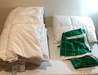 Two white down comforters folded beside green grid duvet cover on bed
