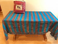 Striped blanket draped over table and packaged travel blanket on top