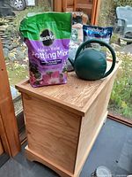 Wooden chest with bags of potting mix, grass seed, fertilizer and watering can on top