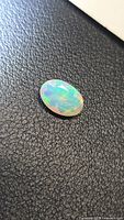 Oval faceted opal on black surface showing multicolor play-of-color