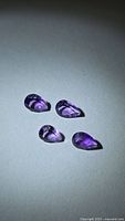 Four pear-cut deep purple amethyst gemstones on neutral background