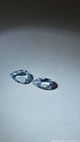Two pear-cut light blue gemstones on neutral background