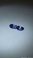 Pair of oval blue-purple tanzanites on neutral background