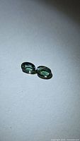 Pair of oval green-blue sapphires on white background