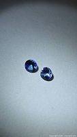 Two round deep blue-purple tanzanite gemstones on neutral background