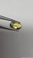 Gemstone held in tweezers, showing oval cut and color