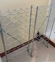 Front view of silver metal wine rack showing three vertical sections and multiple wavy bottle supports