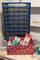 Blue 36-drawer organizer with one drawer missing, red holiday shoebox with fasteners