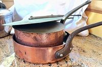 Two nested copper saucepans with cast iron handles and lids