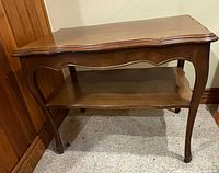 Wooden end table with lower shelf, angled view showing top surface, legs and wear