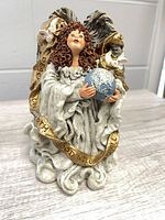Front view of angel figurine holding globe and ribbon text visible