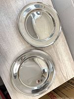 Two silver-tone chargers on wooden surface