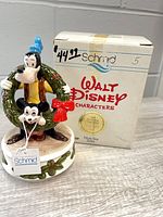 Front view of Goofy holding wreath with Mickey on music box beside original Schmid box