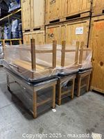 Two Dynatronics tables shrink-wrapped upside down on pallet, shows oak frames and black vinyl tops
