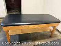 Full view of massage table showing black padded top and wooden frame