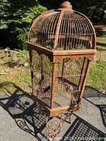 Full view of tall ornate rust-patina metal birdcage on integrated scroll stand