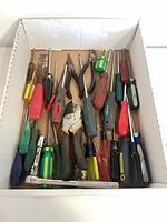 Top view of box containing assorted screwdrivers, pliers, Fiskars pruner and other hand tools