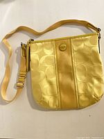 Front view of yellow Coach crossbody bag showing center stripe, logo medallion and adjustable strap