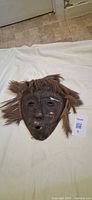 front view of carved wood mask with fiber hair