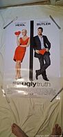 Full view of The Ugly Truth poster on floor held by clips