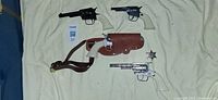 Overview of three toy revolvers, holster with strap, sheriff badge
