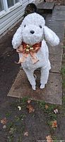 Front view of white flocked poodle statue with ribbon and bells