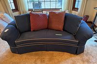 Front view of curved navy blue sofa with tan piping and two red pillows