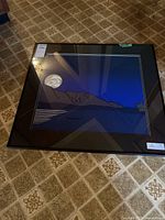 Full view of framed print on floor showing artwork, frame, and glass